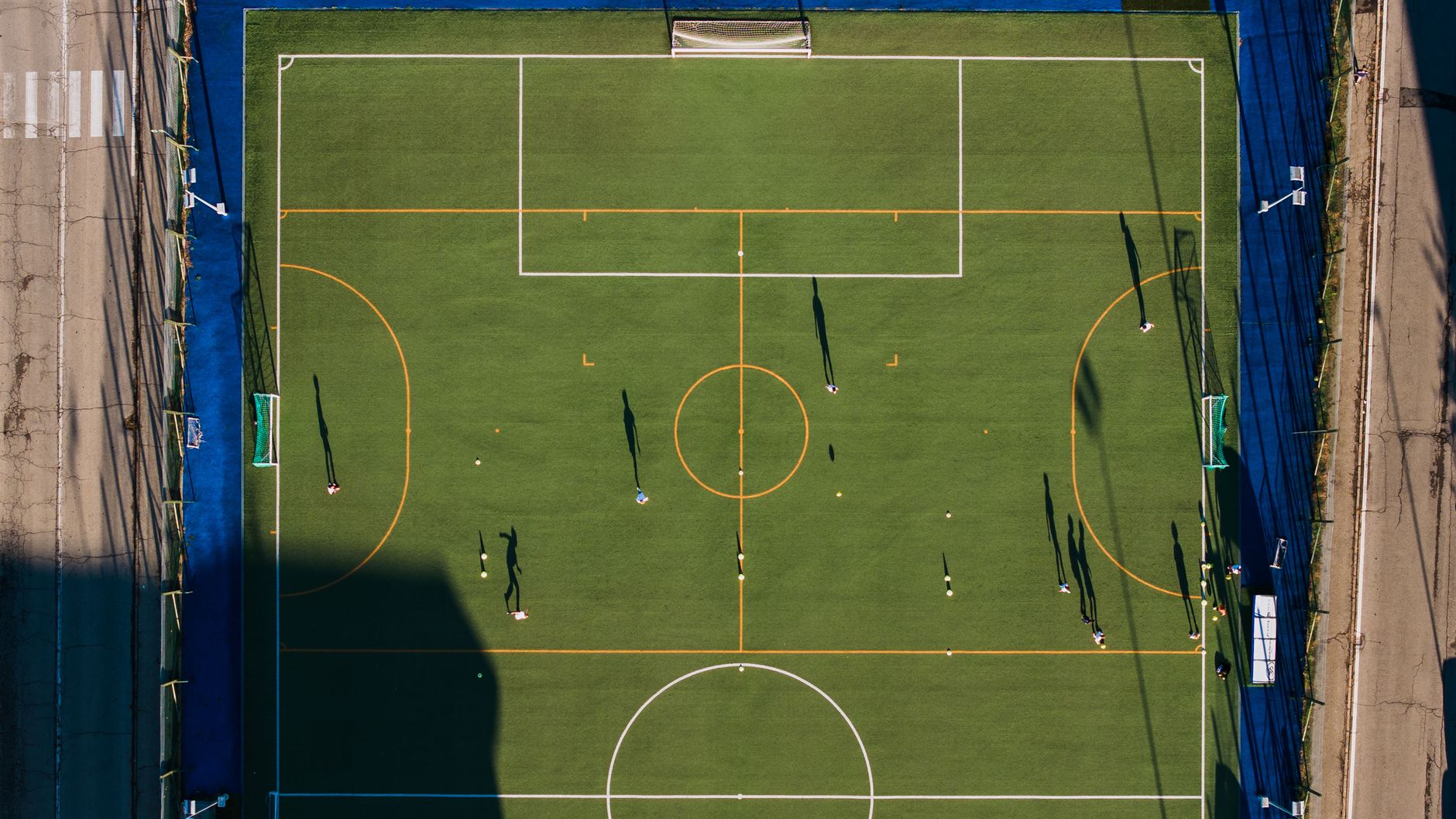 Aerial view of a soccer match on a green field in Alba, showcasing players and shadows.