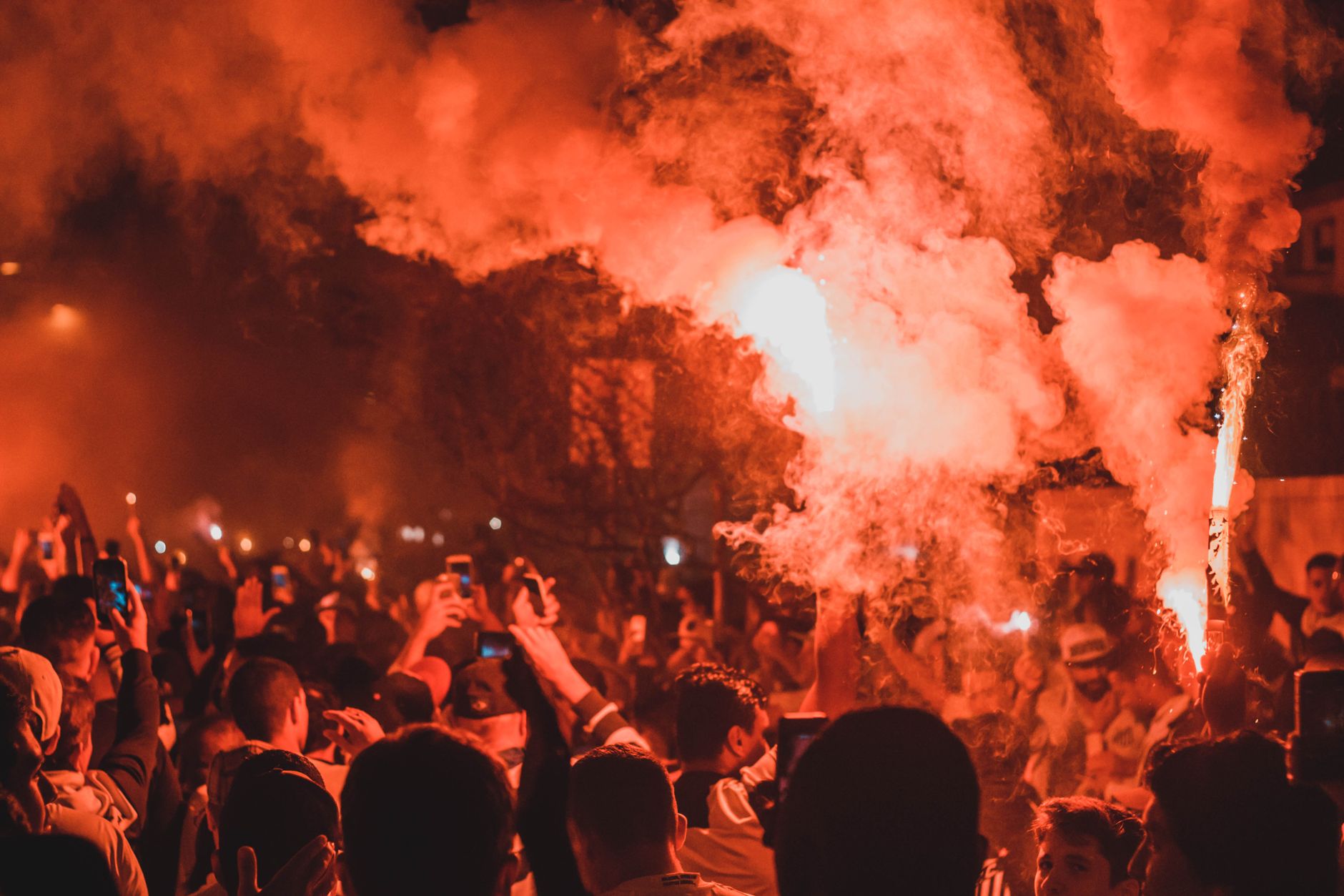 Crowd of unrecognizable activists with burning torches standing on street among smoke during demonstrations at night