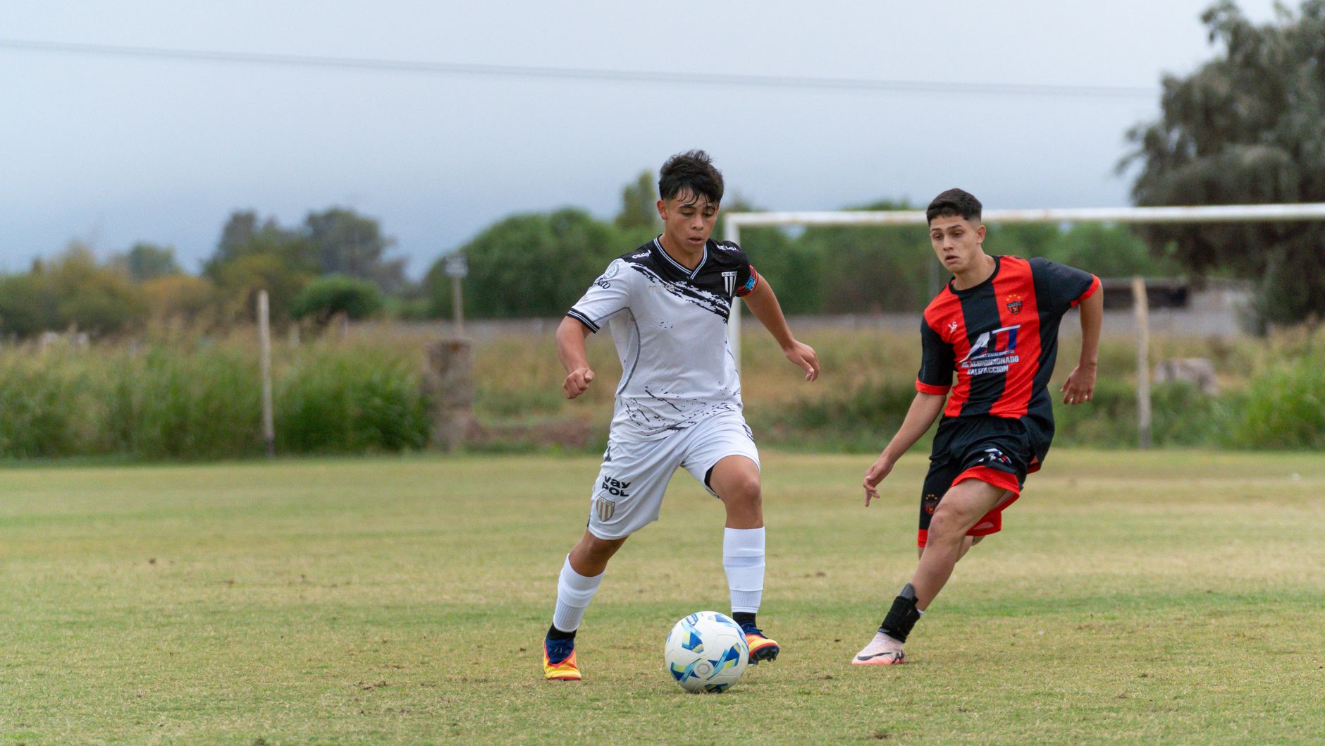 Two teenage soccer players in uniforms compete on an outdoor field.