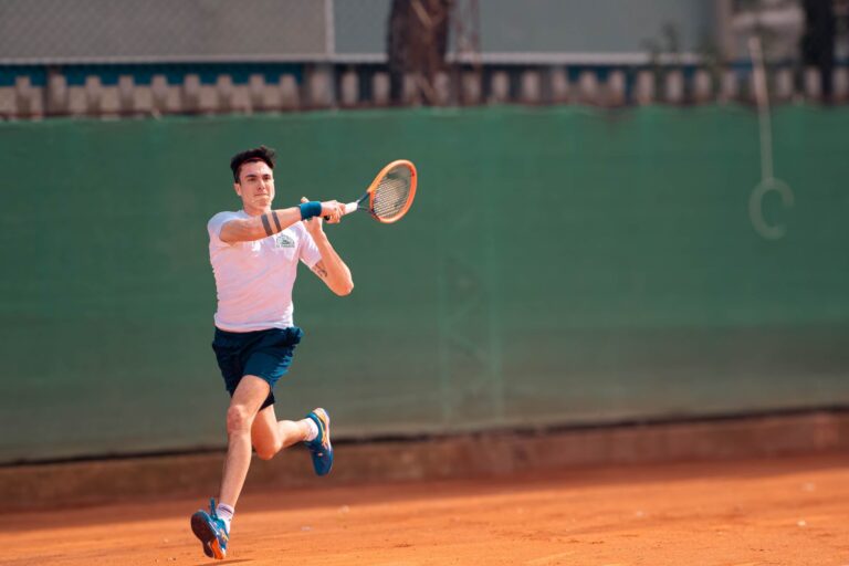 Dynamic shot of a male tennis player in motion on a clay court during a match.