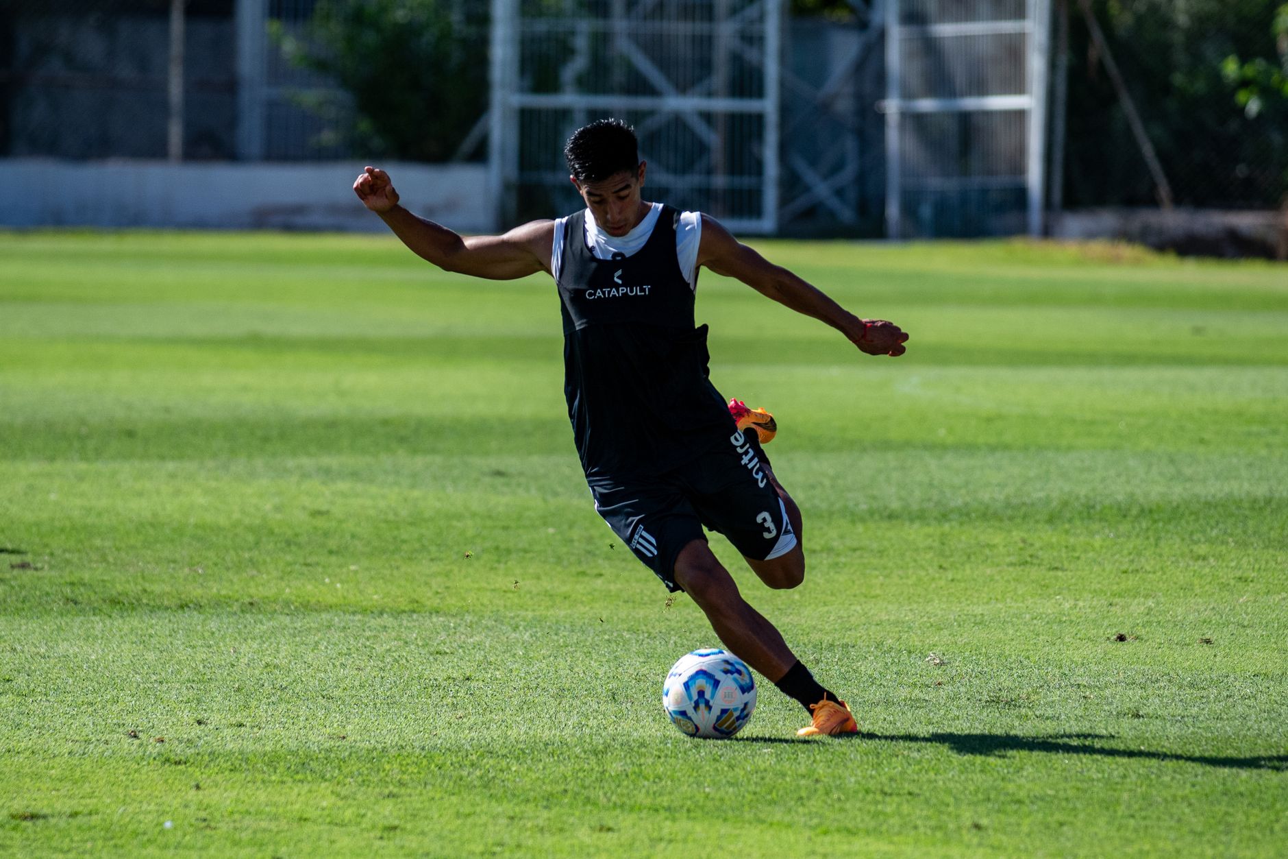 A teenage soccer player in action on a green field during daytime practice.