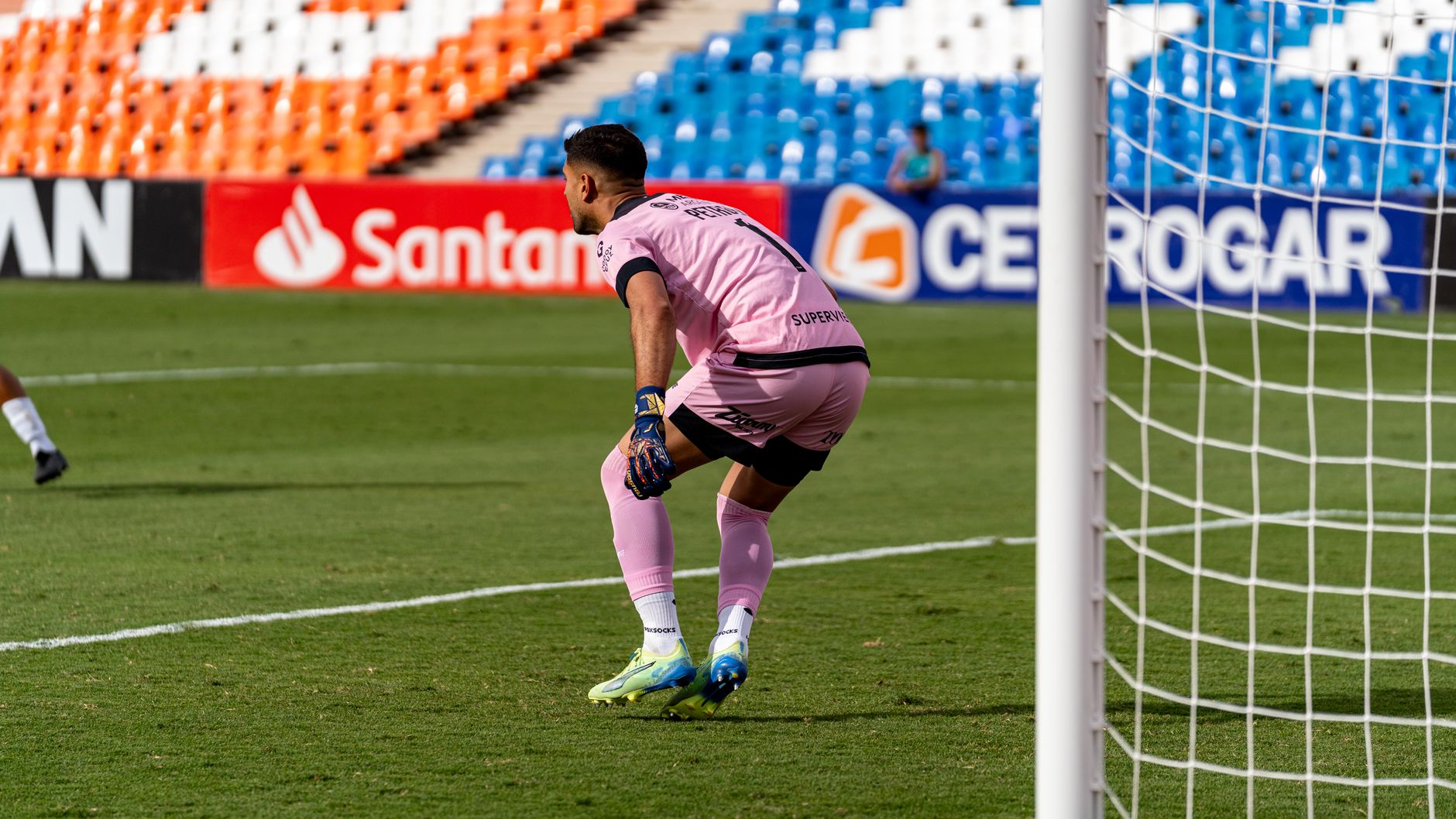 Soccer goalkeeper in pink uniform focuses during a match.