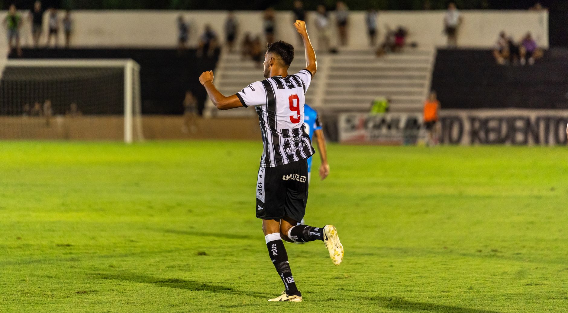 Soccer player in black and white jersey celebrates a goal on the field at night.