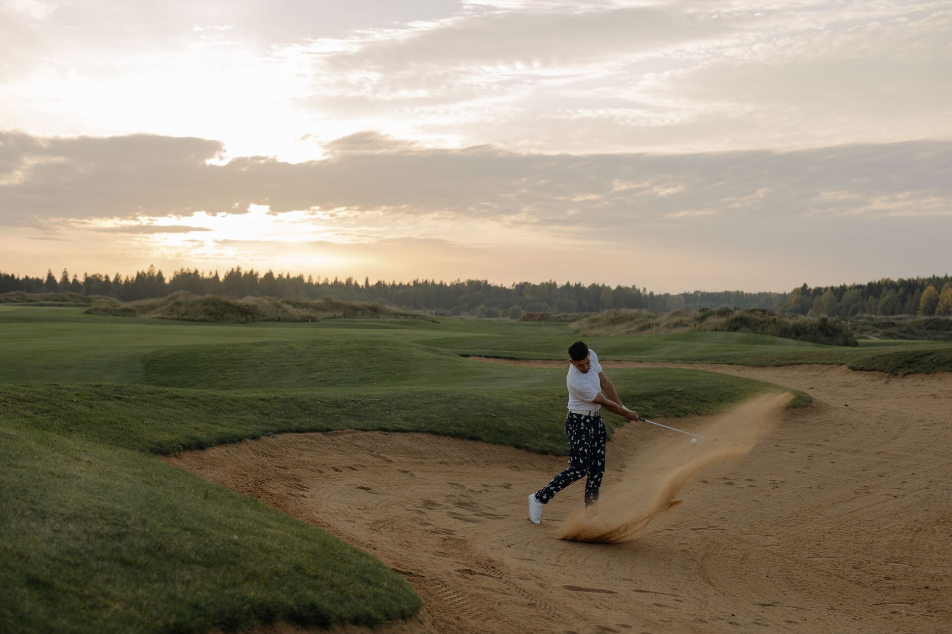 Golfer hitting a sand shot at sunset on a scenic golf course, showcasing skill and landscape.