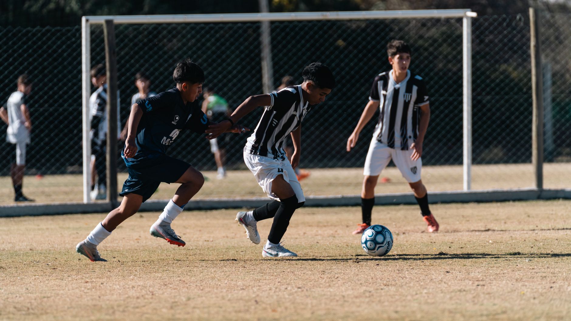 Teen boys in active play during a competitive soccer match on a sunny day.
