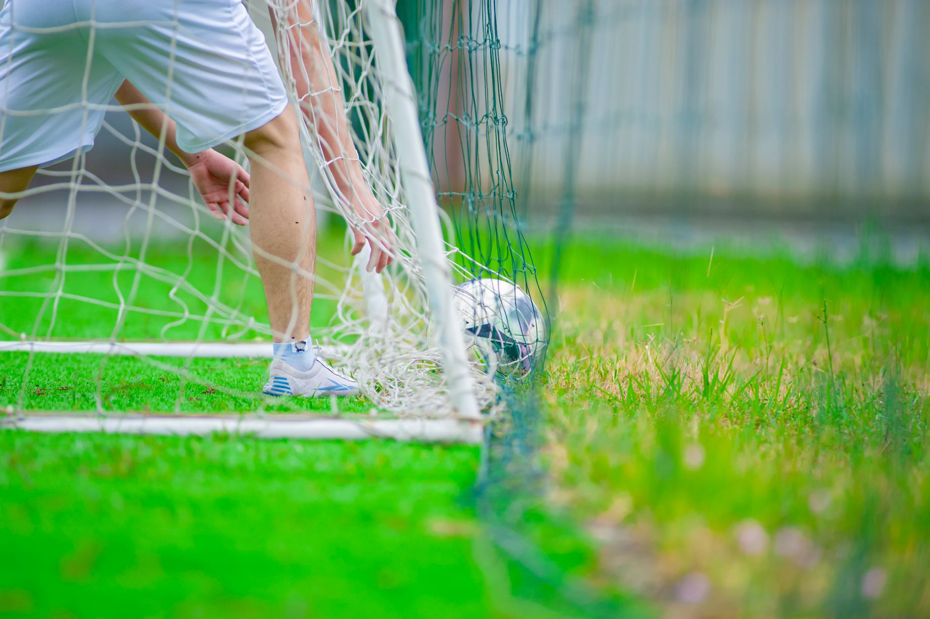 A soccer player retrieves a ball from the goal on a lush green field, captured in Hanoi, Vietnam.
