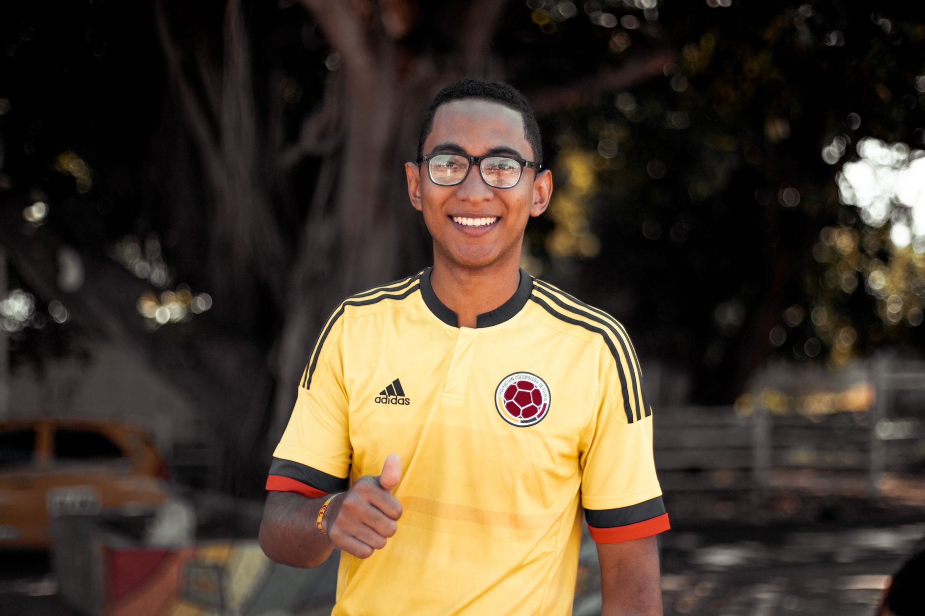Smiling man wearing a sports jersey outdoors, giving a thumbs-up gesture.