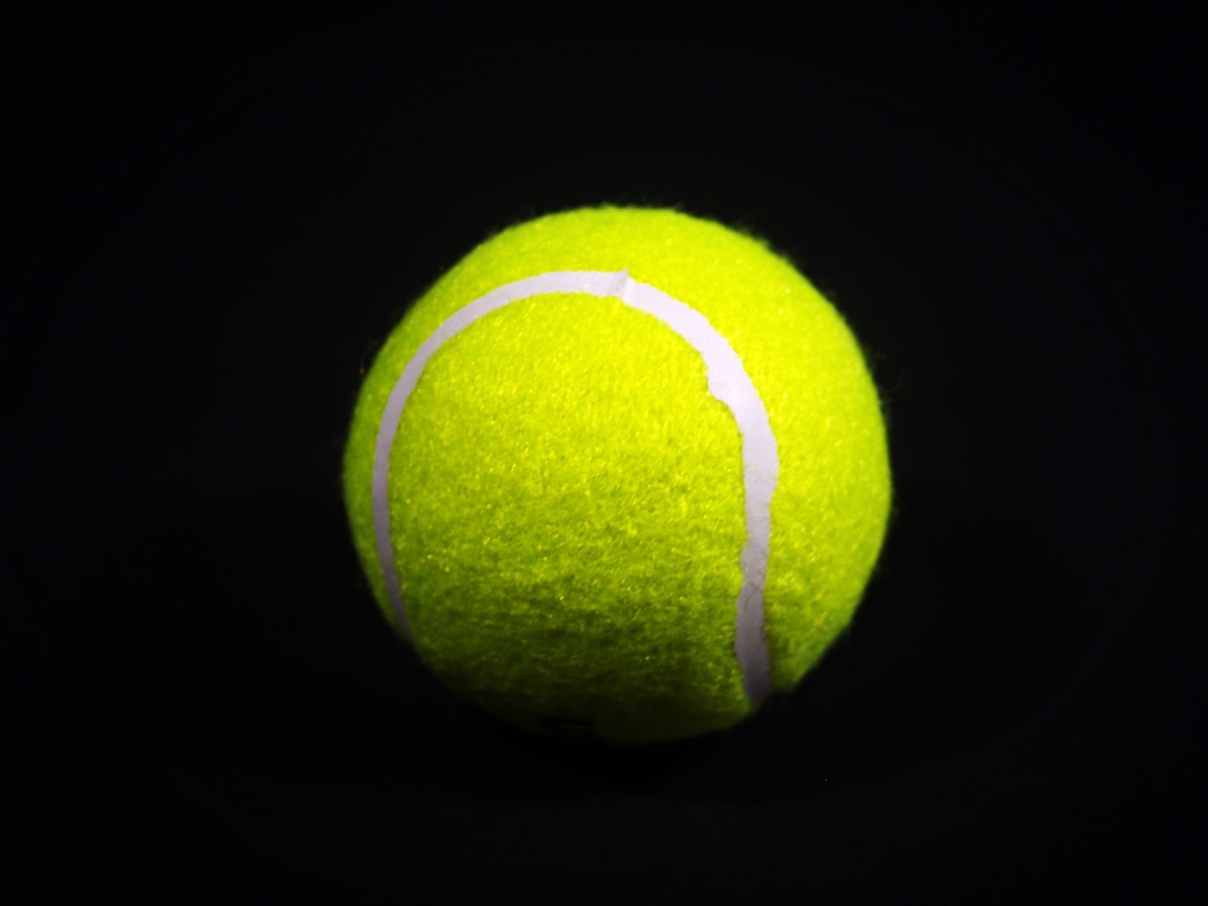 Close-up of a bright yellow tennis ball against a dark background, highlighting texture and color contrast.