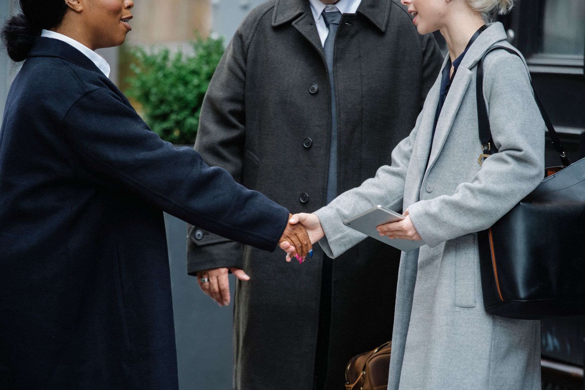 Crop anonymous diverse businesswomen in trendy elegant coats shaking hands after important conference on street