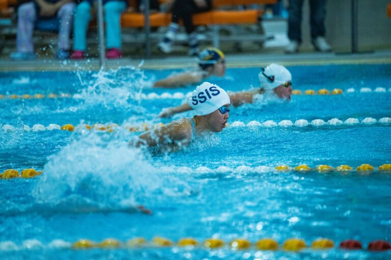 Athletes in a competitive swimming race at an indoor pool.