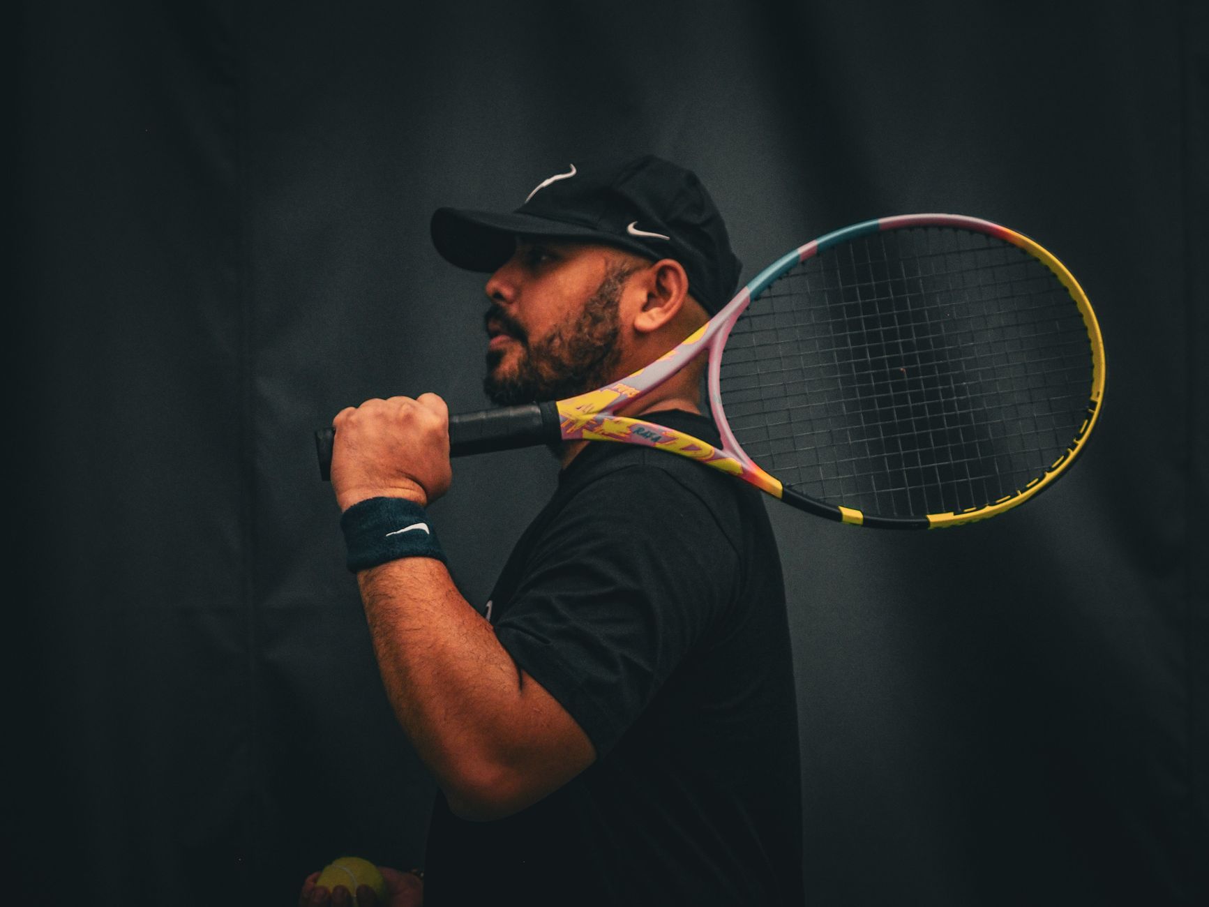 Portrait of a focused male tennis player holding a racket against a dark background.