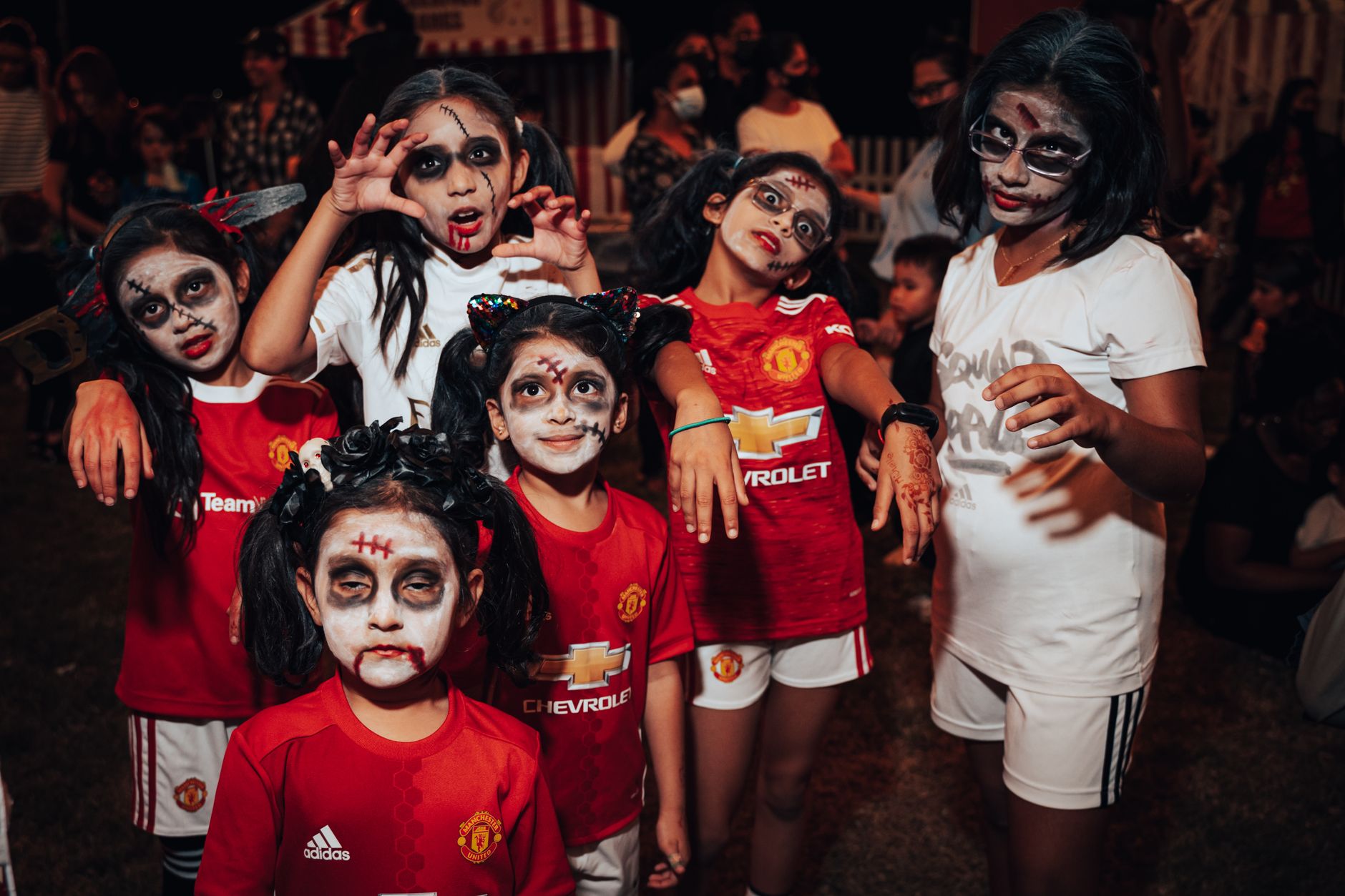 Group of kids in zombie makeup enjoying a Halloween celebration outdoors at night.