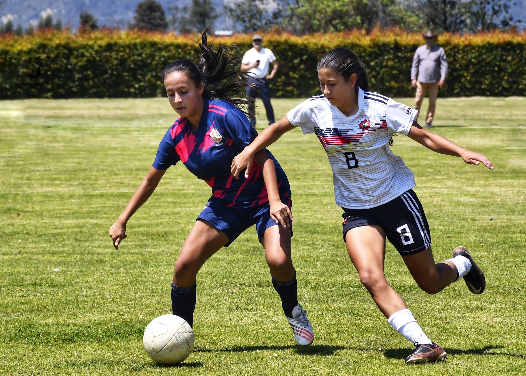 Two female soccer players competing fiercely on a sunny day outdoors.