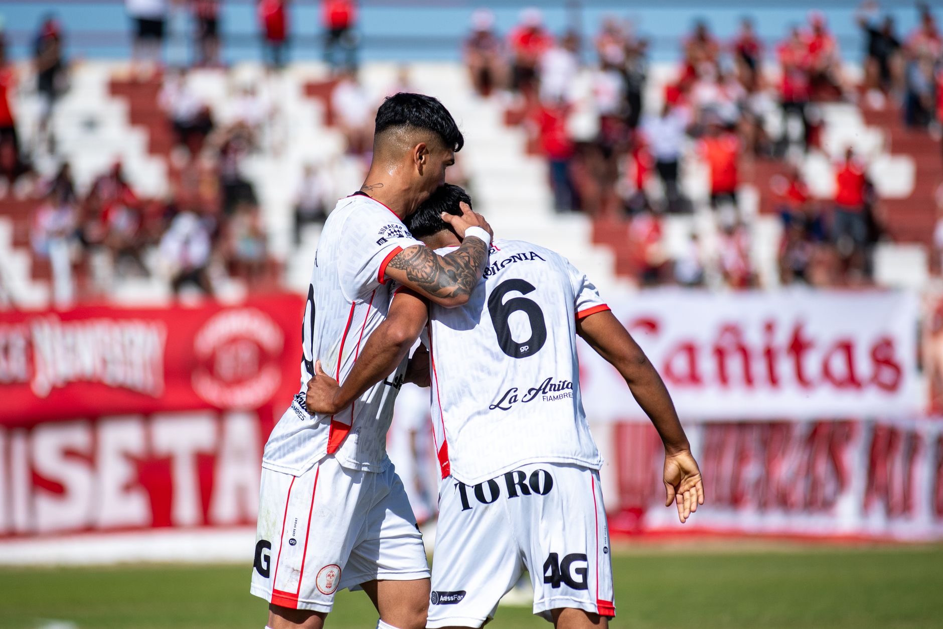 Two soccer players celebrating a goal with a crowd in the background.