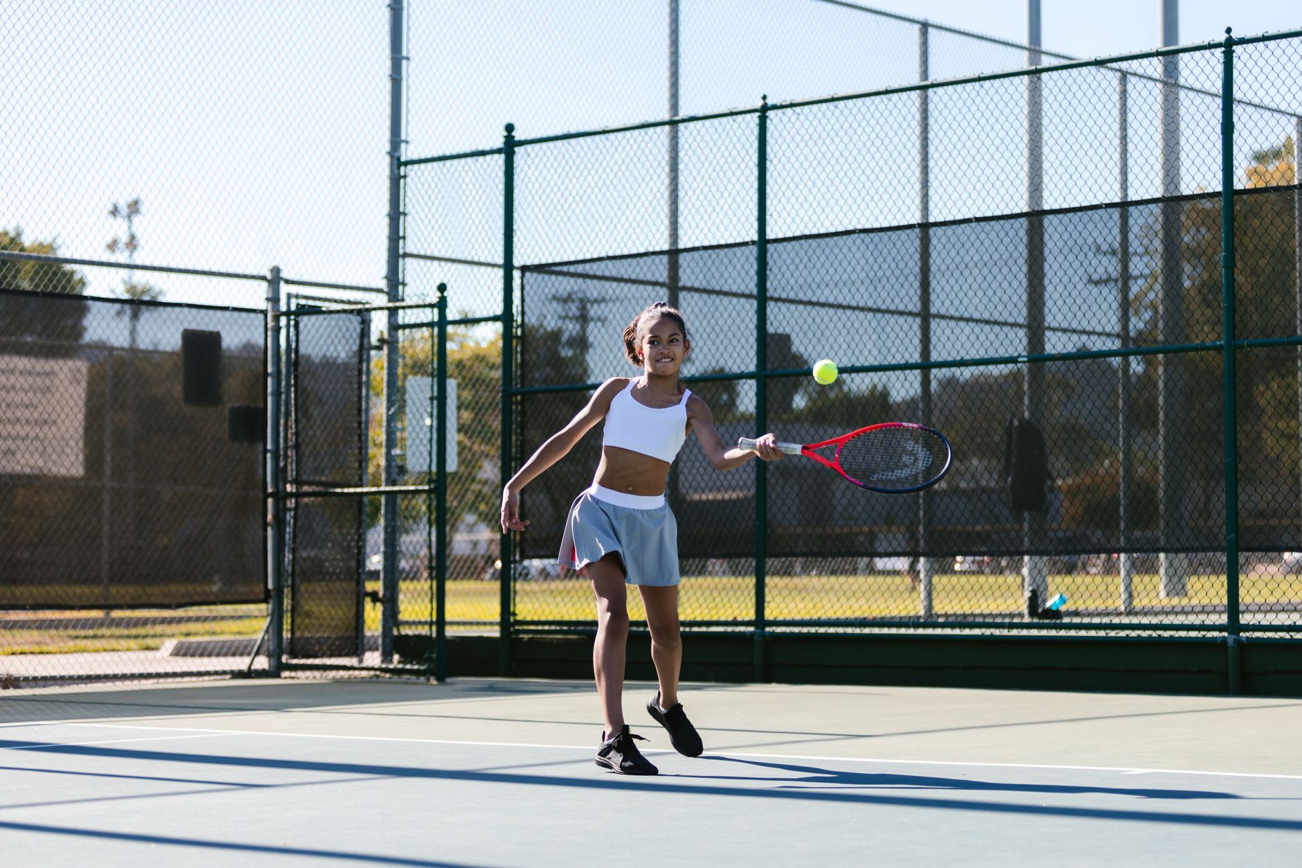 A young girl joyfully practicing tennis on an outdoor court during the day.