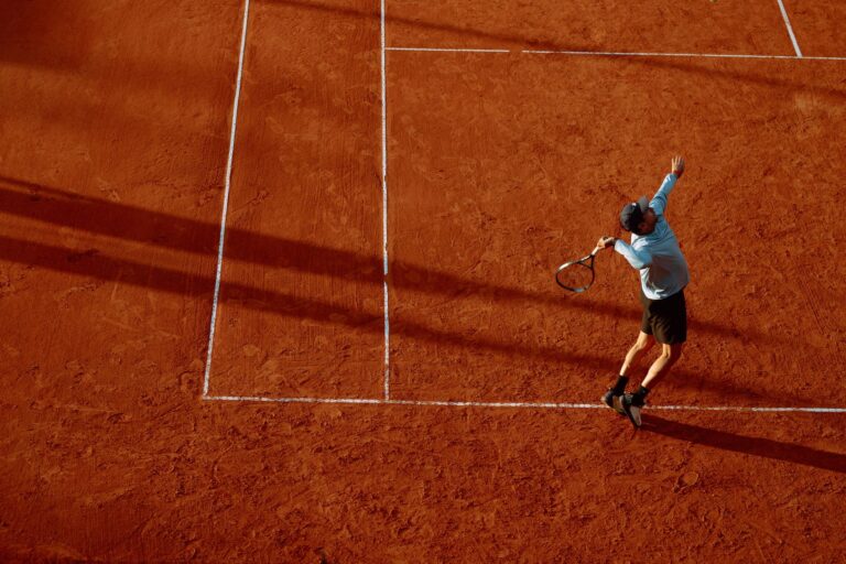 A dynamic shot of a tennis player serving on a clay court during sunset.