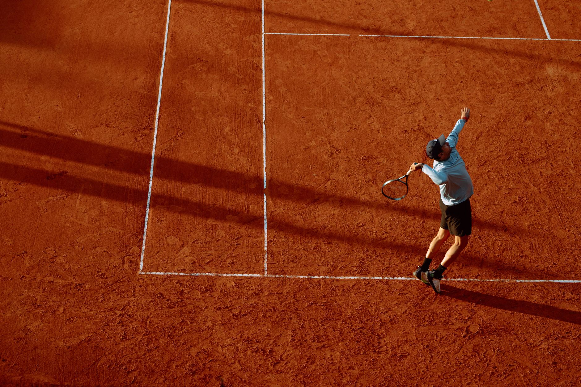 A dynamic shot of a tennis player serving on a clay court during sunset.