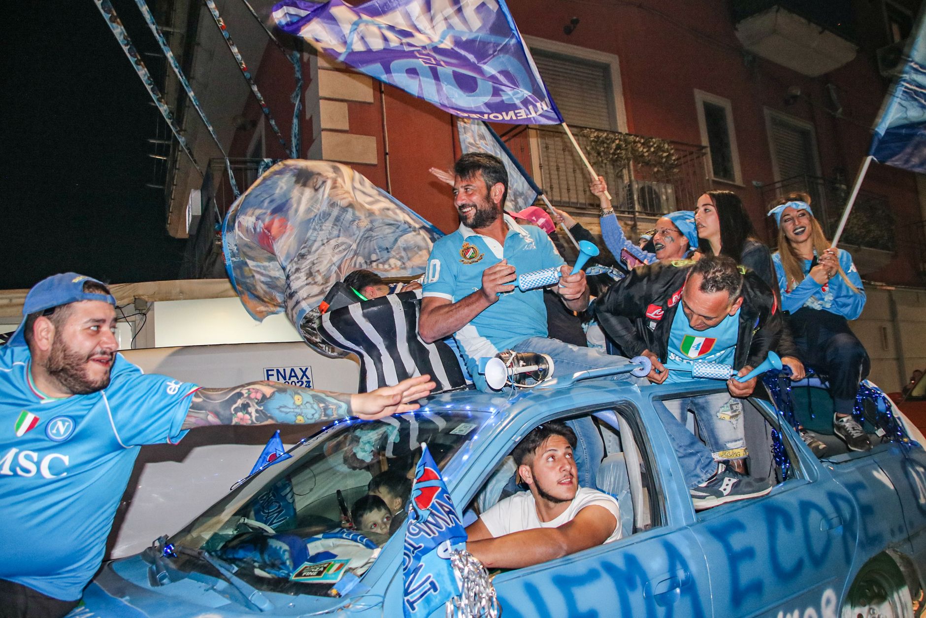 Excited fans celebrate a sports victory in the streets of Pozzuoli, Italy with flags and cheers.