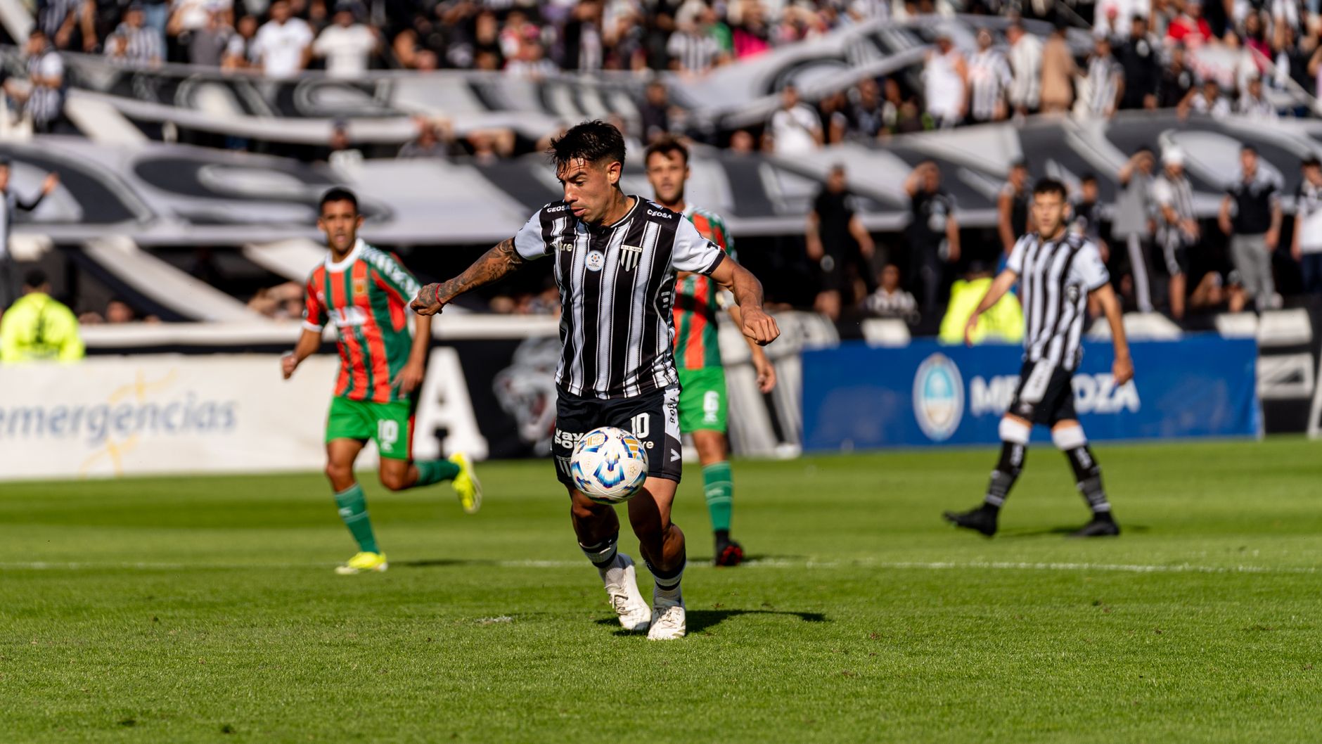 Football players in action during an intense outdoor match with a vibrant crowd in the background.