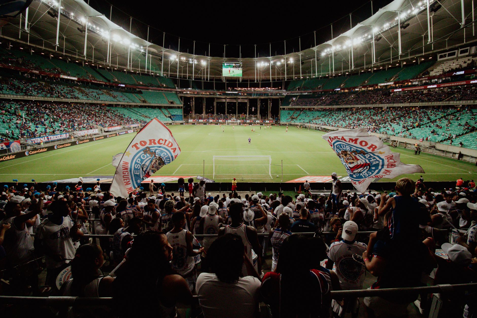 Energetic soccer fans cheer during a night match at a large stadium, creating an exciting atmosphere.