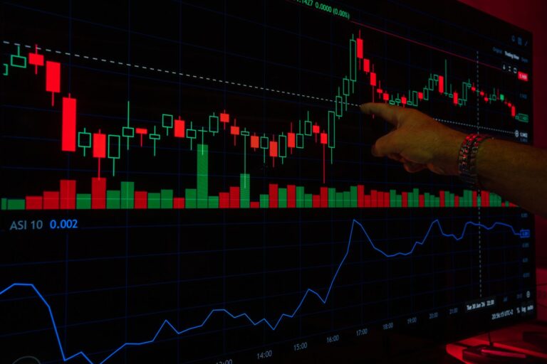 A hand points at a stock market graph on a digital screen, highlighting financial trading trends.