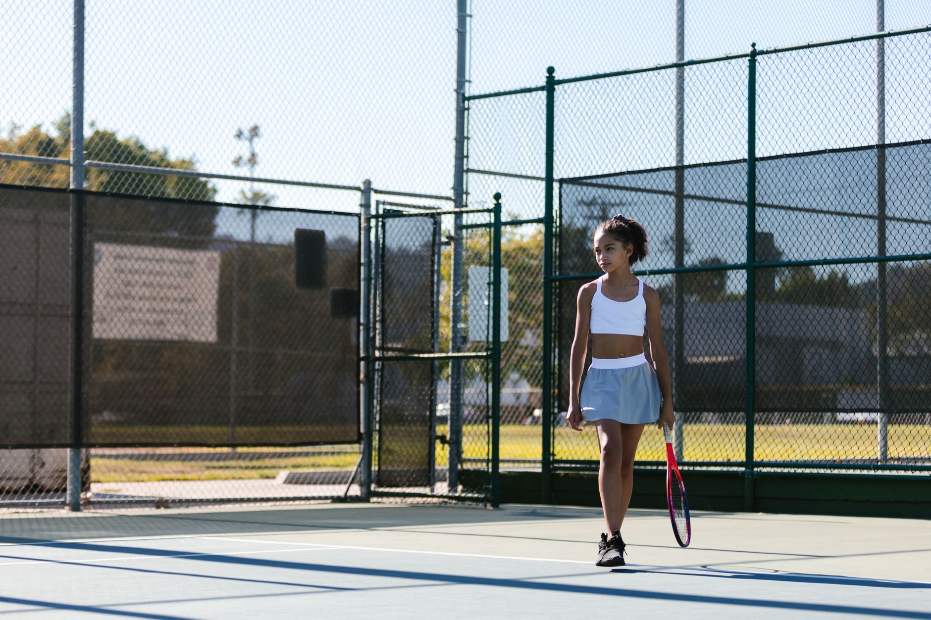 A young girl prepares for tennis practice on an outdoor court, holding a tennis racket.