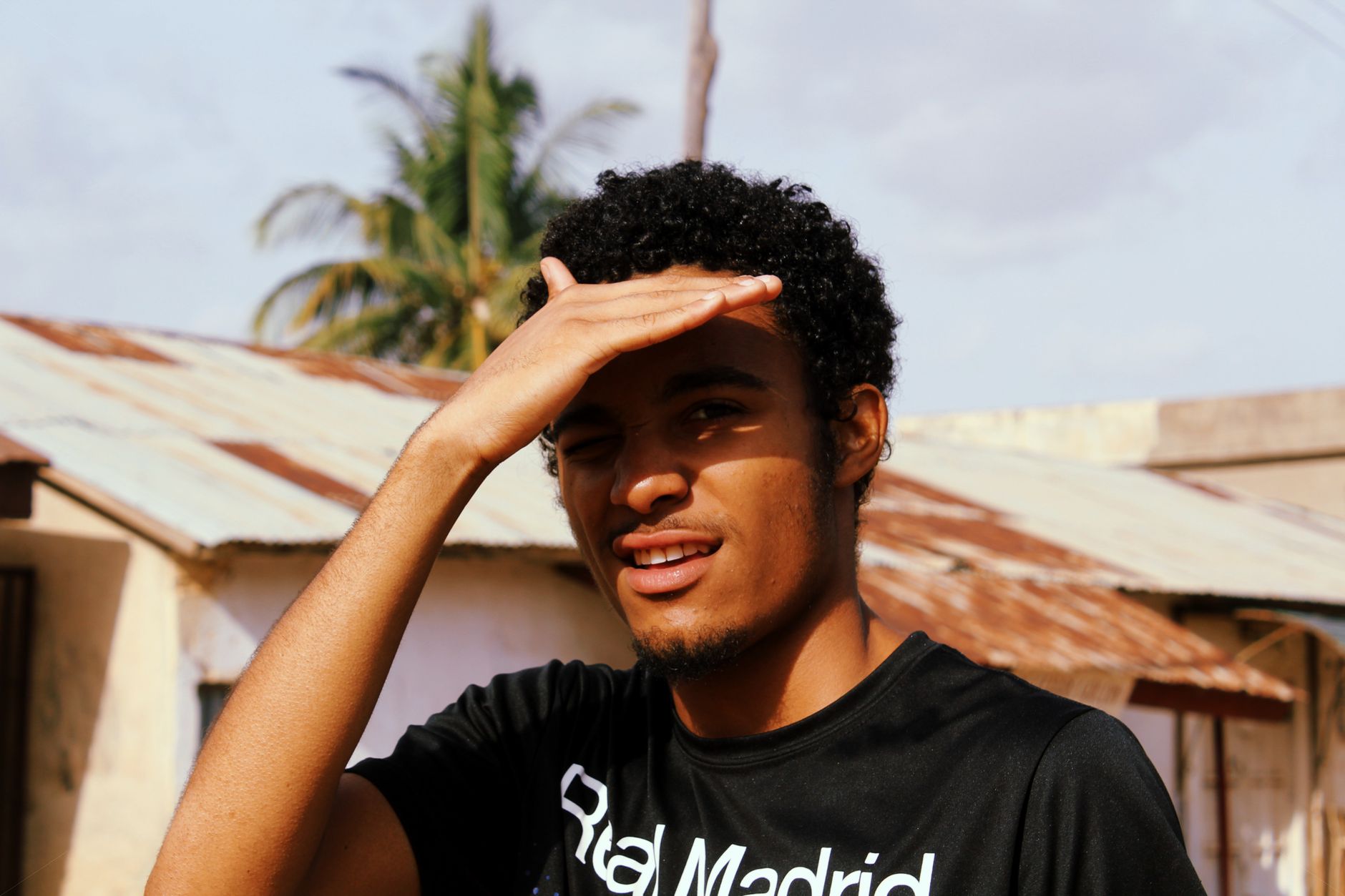 Portrait of an African man shielding his eyes from the sun in a rustic outdoor setting.