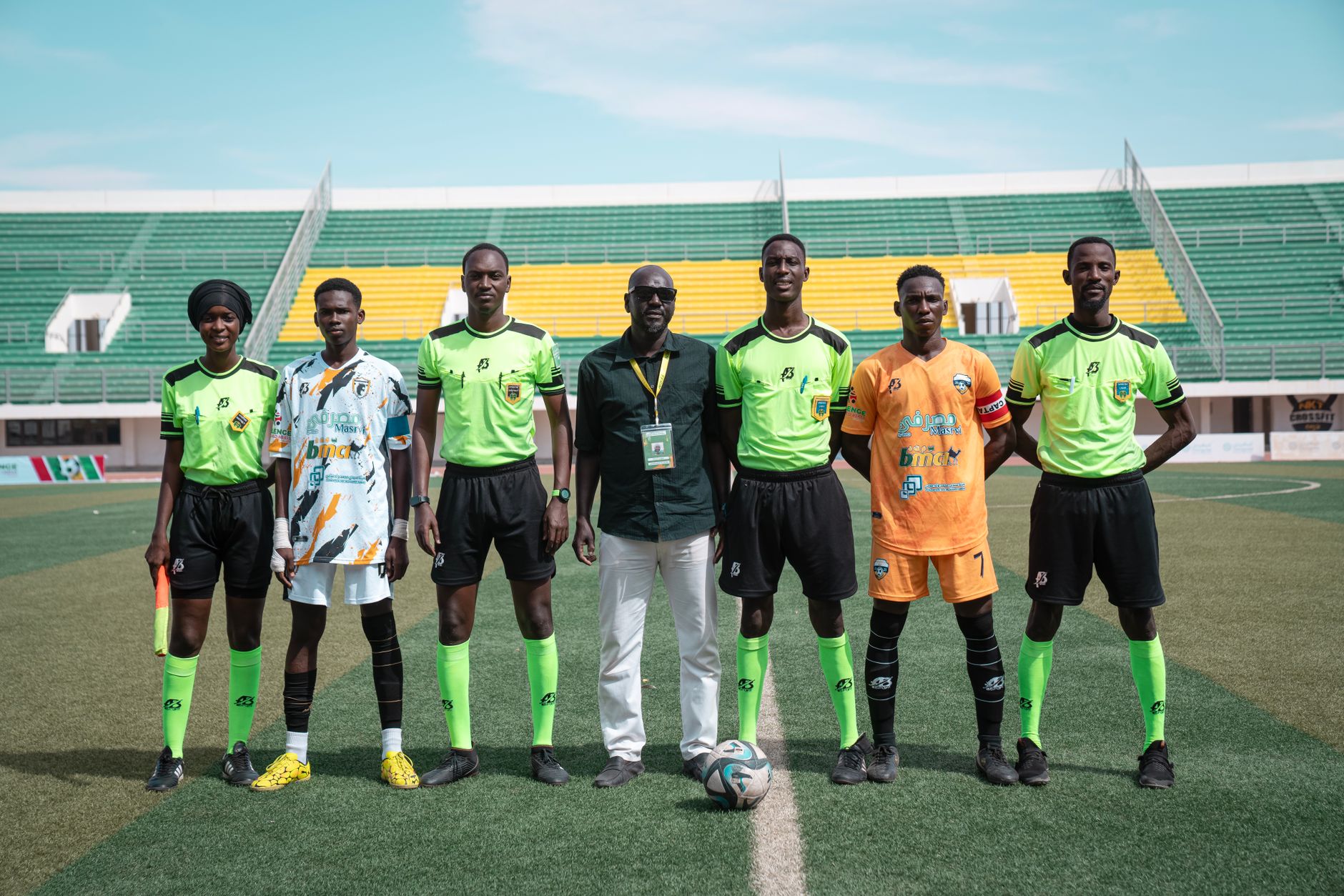 A soccer team with officials posing on a field during daytime at a stadium.