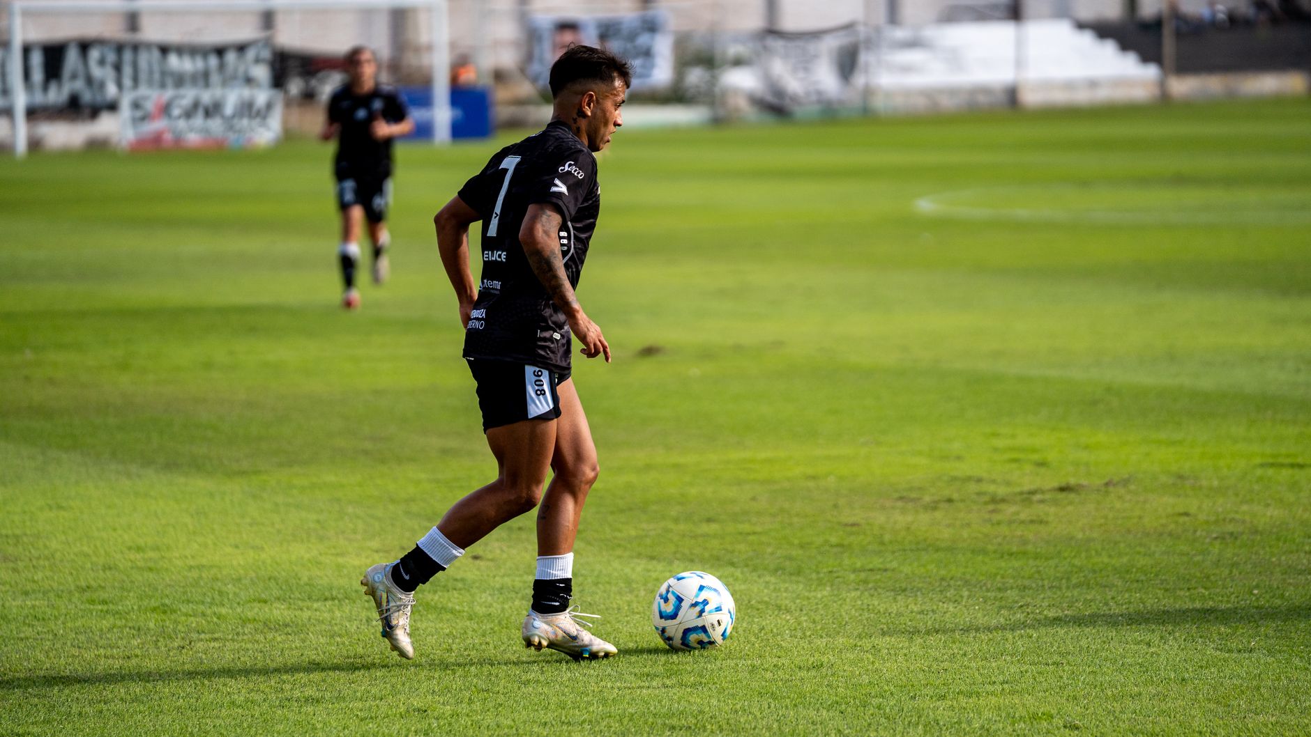 Soccer player dribbling ball during a match on a sunny day.