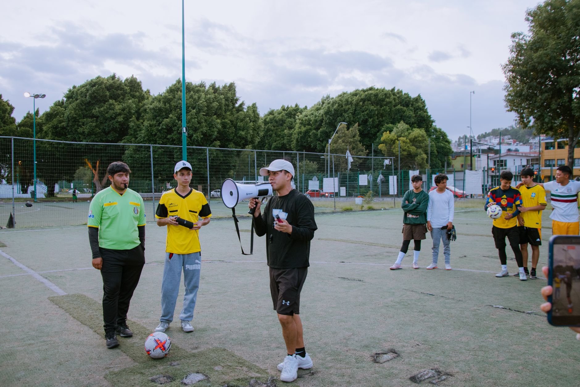 A soccer coach instructs young players on an outdoor field during the day.