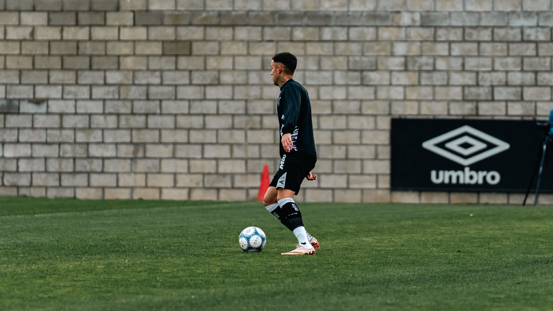 Soccer player practicing on a grass field with a brick wall backdrop, showcasing athletic talent.
