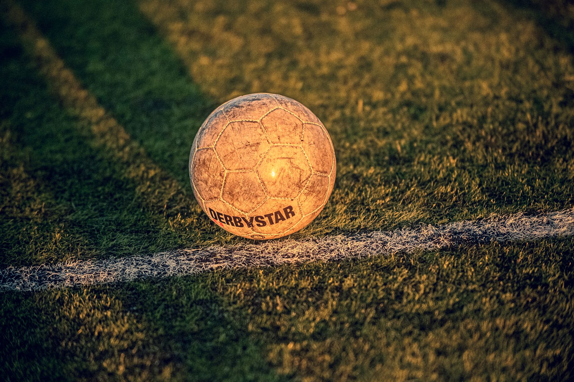 Close-up of a worn soccer ball on a grassy field during sunset, capturing the essence of play.
