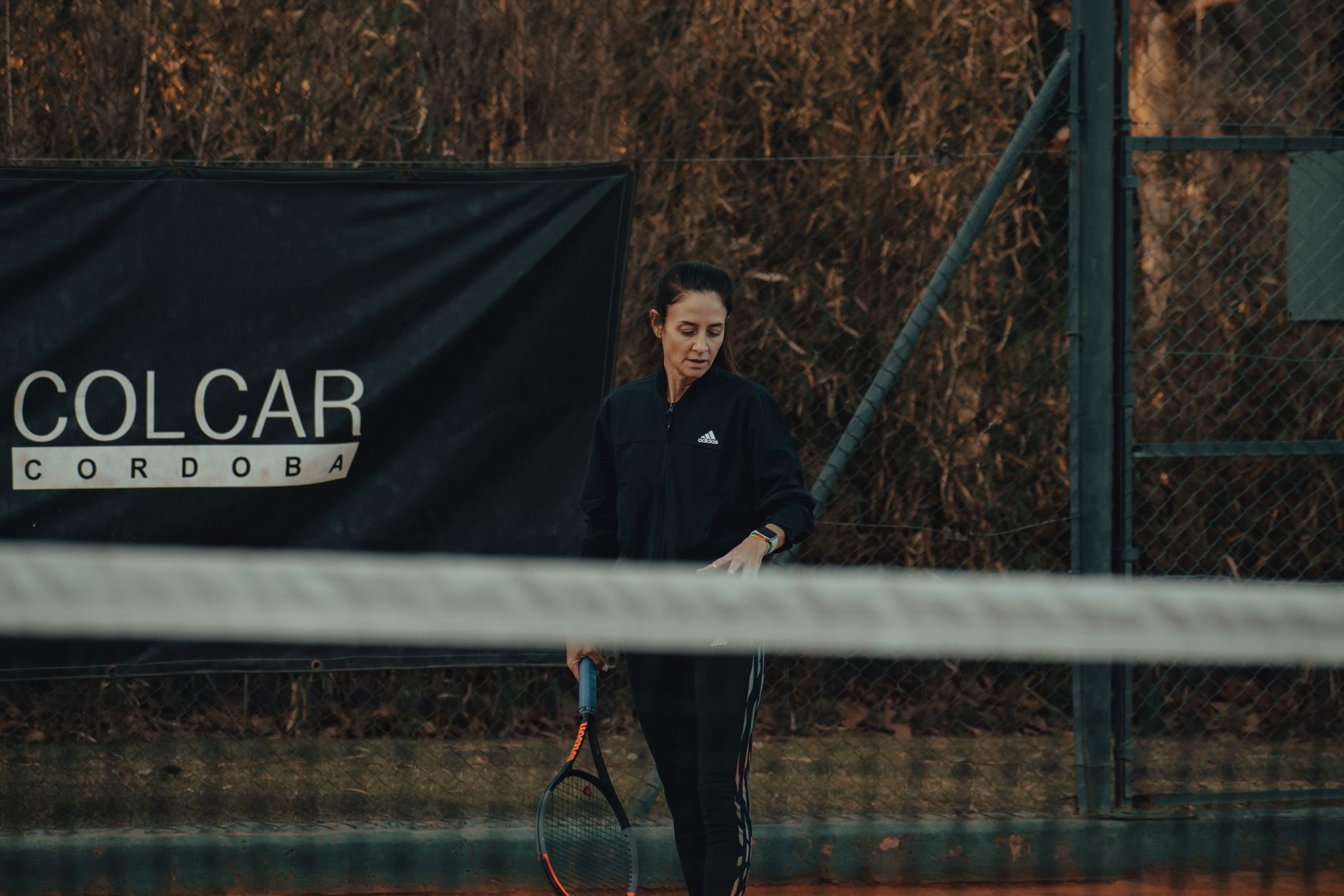 A woman holding a tennis racket on an outdoor clay tennis court next to a COLCAR CORDOBA sign.