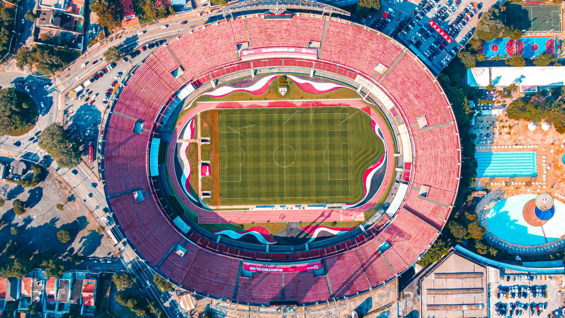 High-angle aerial shot of Morumbi Stadium in São Paulo, featuring the vibrant green field and red seating.