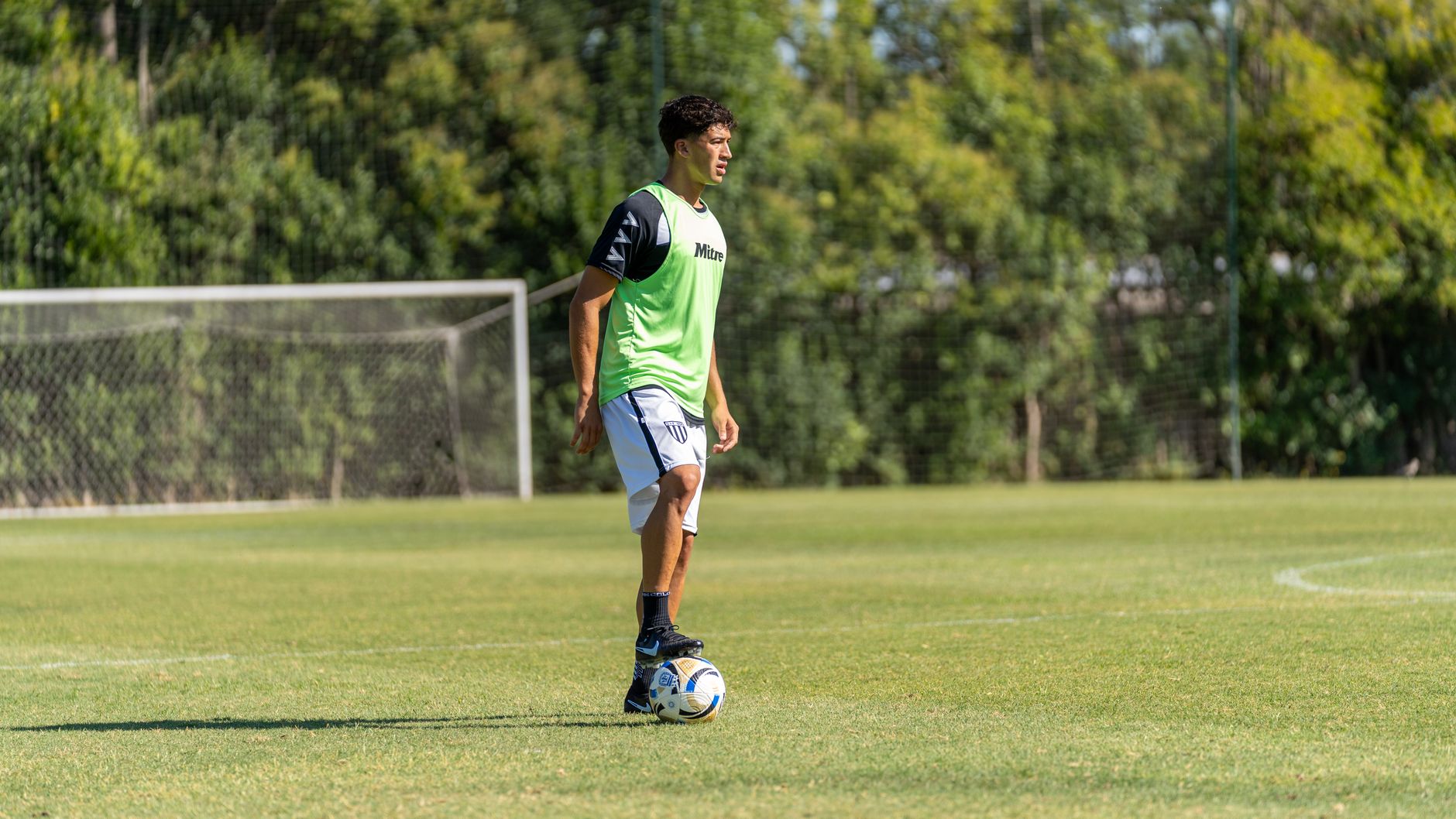A young male soccer player dribbling on a sunny outdoor field during a practice session.