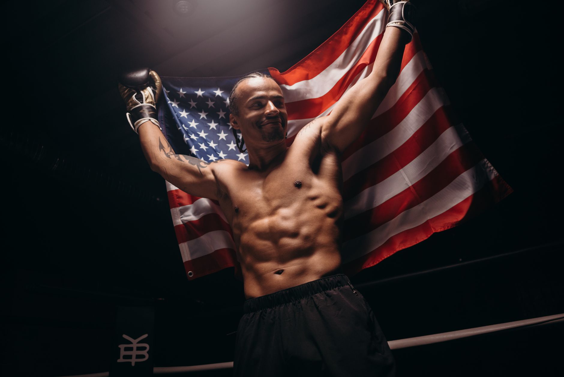 Muscular male boxer celebrates victory with American flag in the boxing ring.