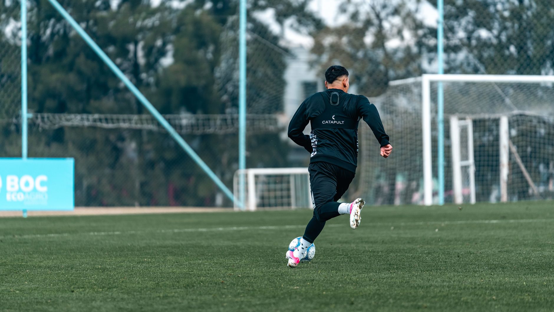 Football player practices dribbling on a professional outdoor field, emphasizing athleticism and skill.