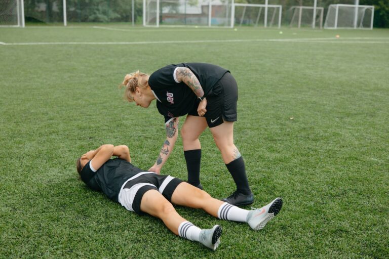 A female soccer player helps an injured teammate on a green soccer field during a game.