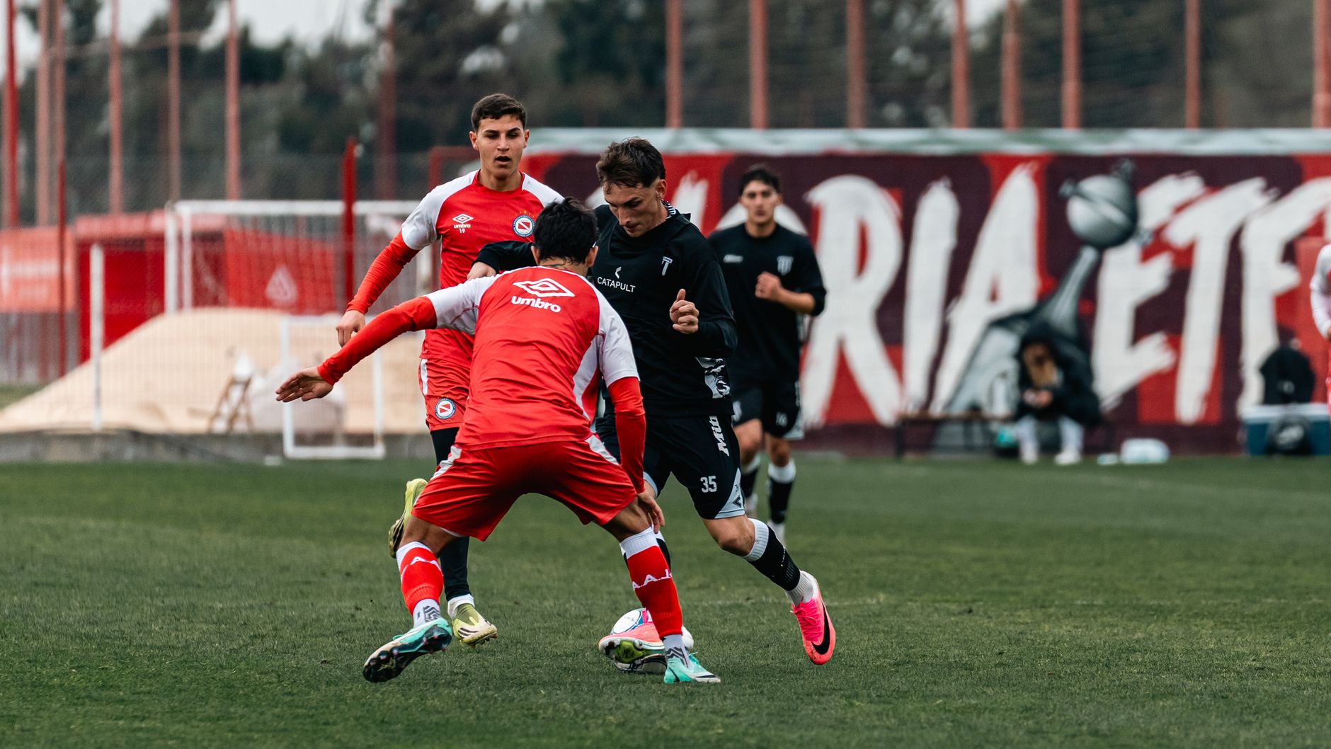 Dynamic soccer match showcasing youth players in red and black jerseys on a field.