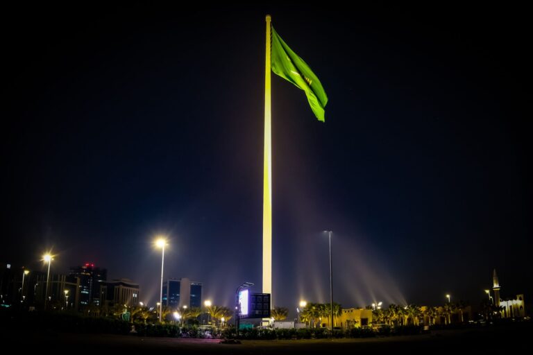 Majestic Saudi Arabian flag illuminated against the night sky, surrounded by cityscape lights in Riyadh.