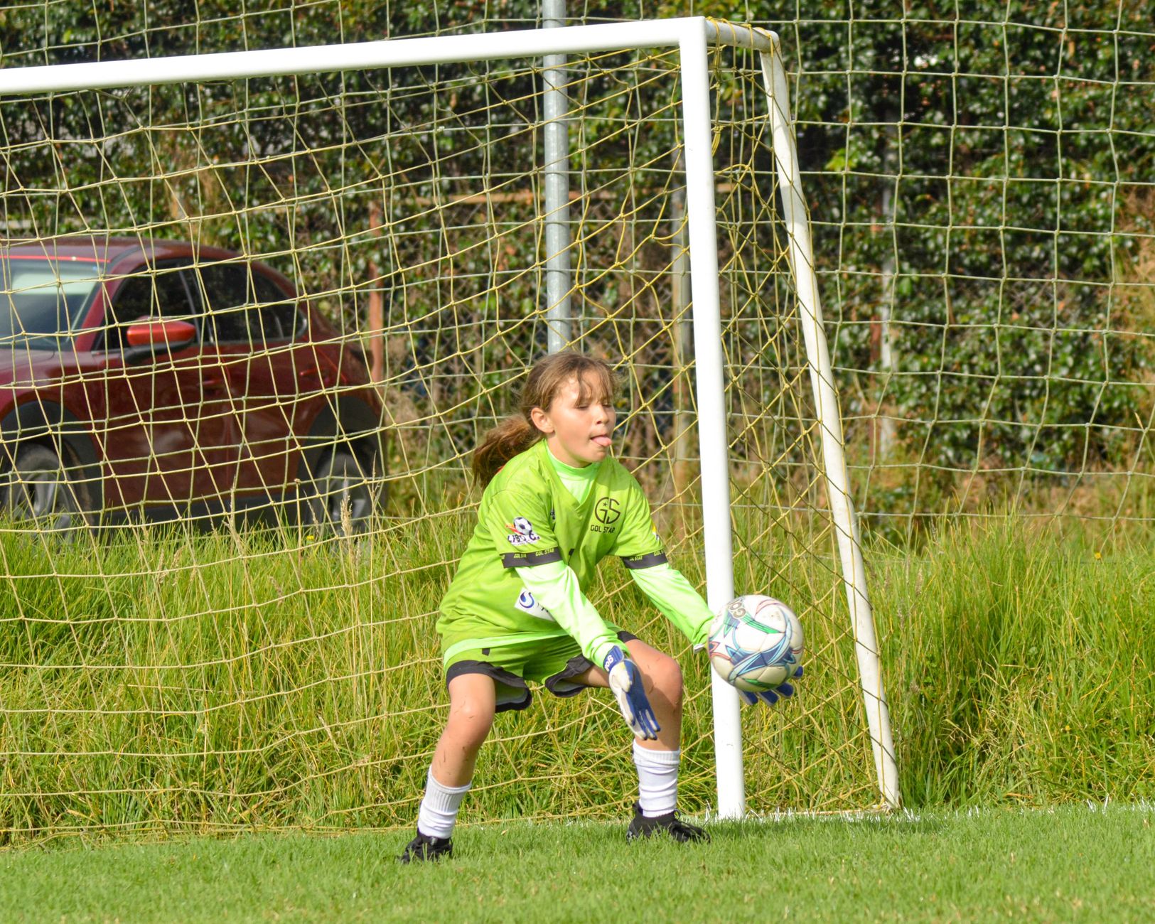 Youth soccer goalie makes a save outdoors on a sunny day.