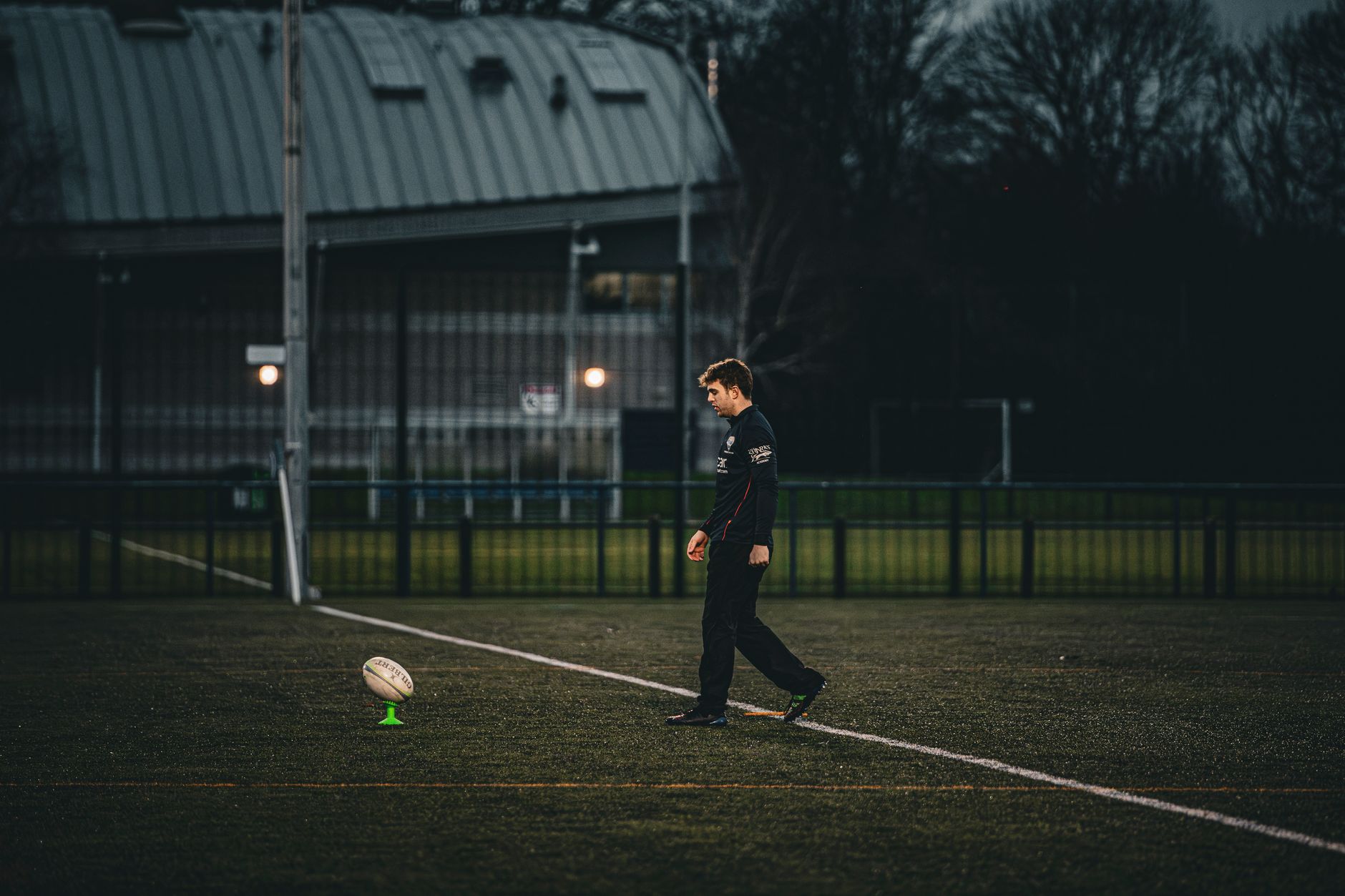 Rugby player sets up for a kick on an empty field in England.