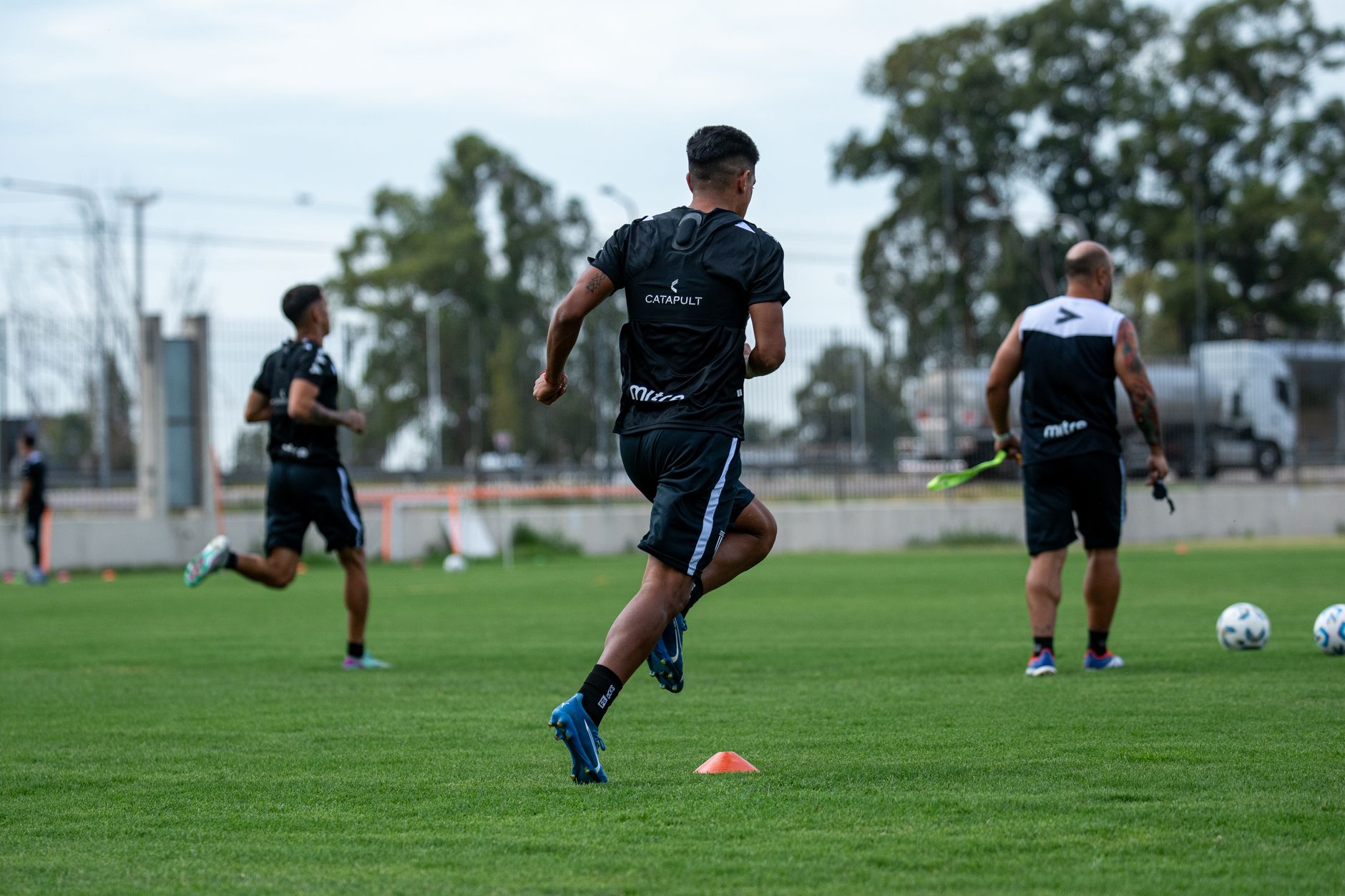 Group of men training on a field, engaging in soccer practice drills in outdoor setting.