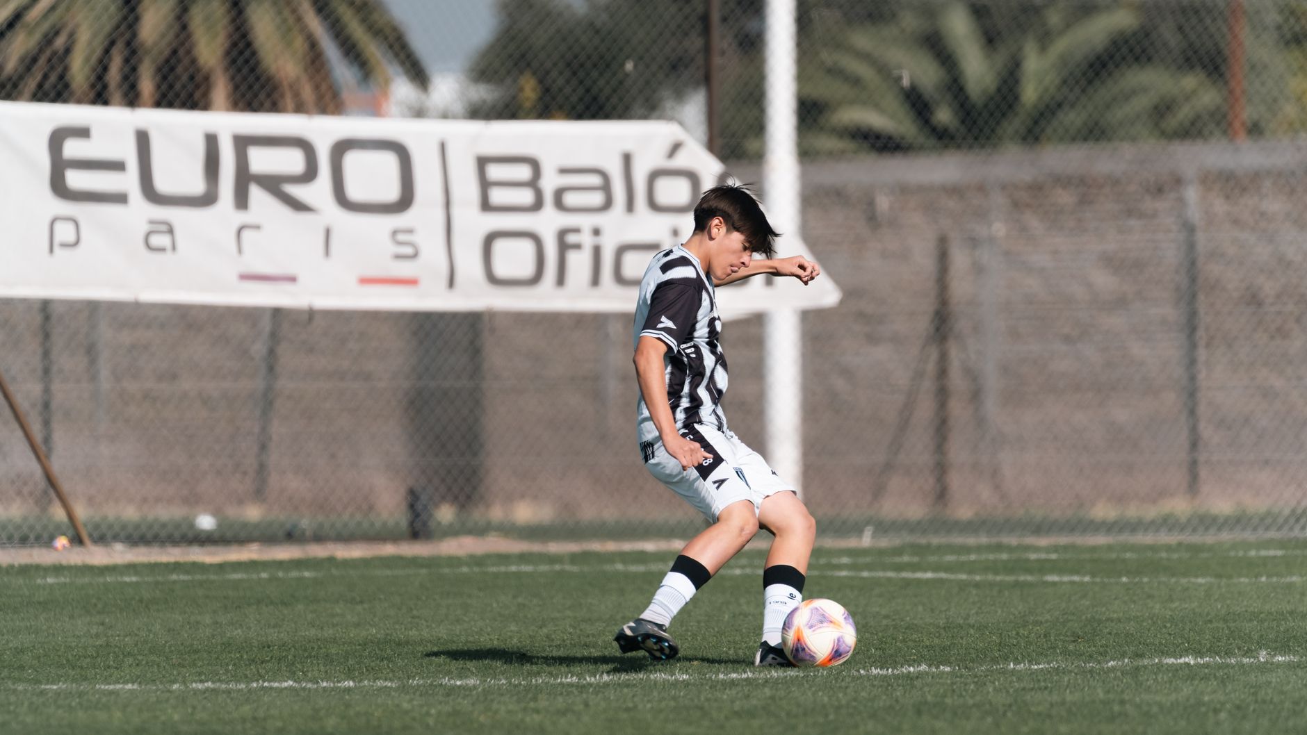 Teen boy in action striking a soccer ball on a grassy field under bright daylight.