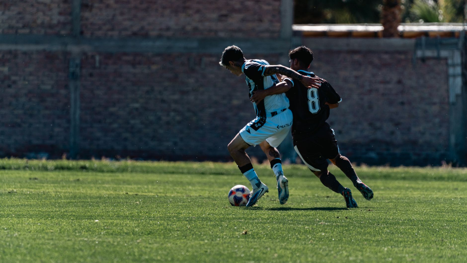 Two soccer players vie for possession during a daytime match.