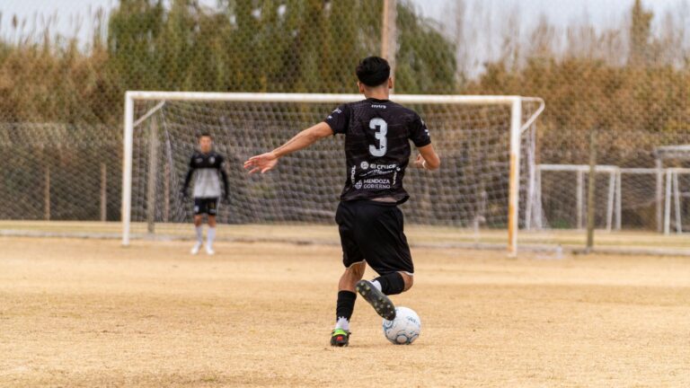 Soccer player in action kicking ball towards goal during outdoor practice.