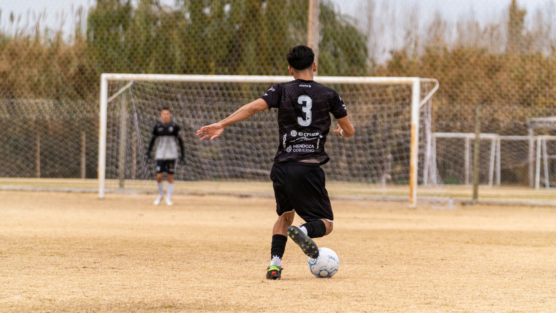 Soccer player in action kicking ball towards goal during outdoor practice.
