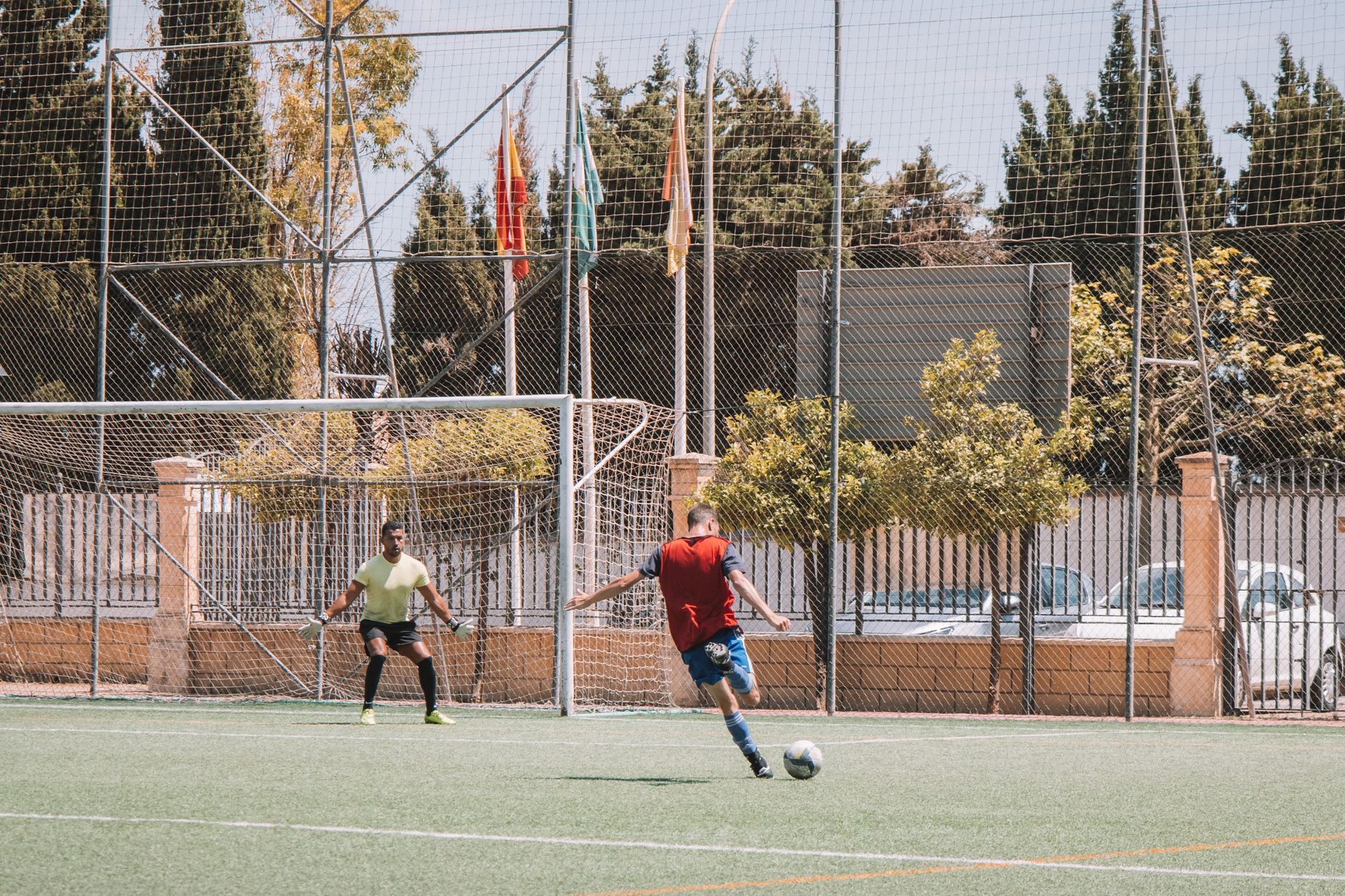 Dynamic soccer match in Málaga, Spain showing player kicking towards goal on sunny day.
