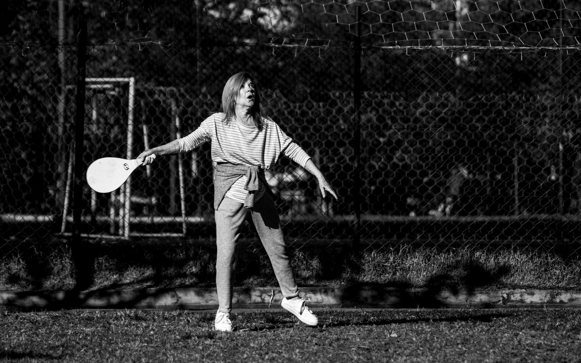 Black and white photo of a woman playing paddle tennis in Buenos Aires, captured in an urban park setting.