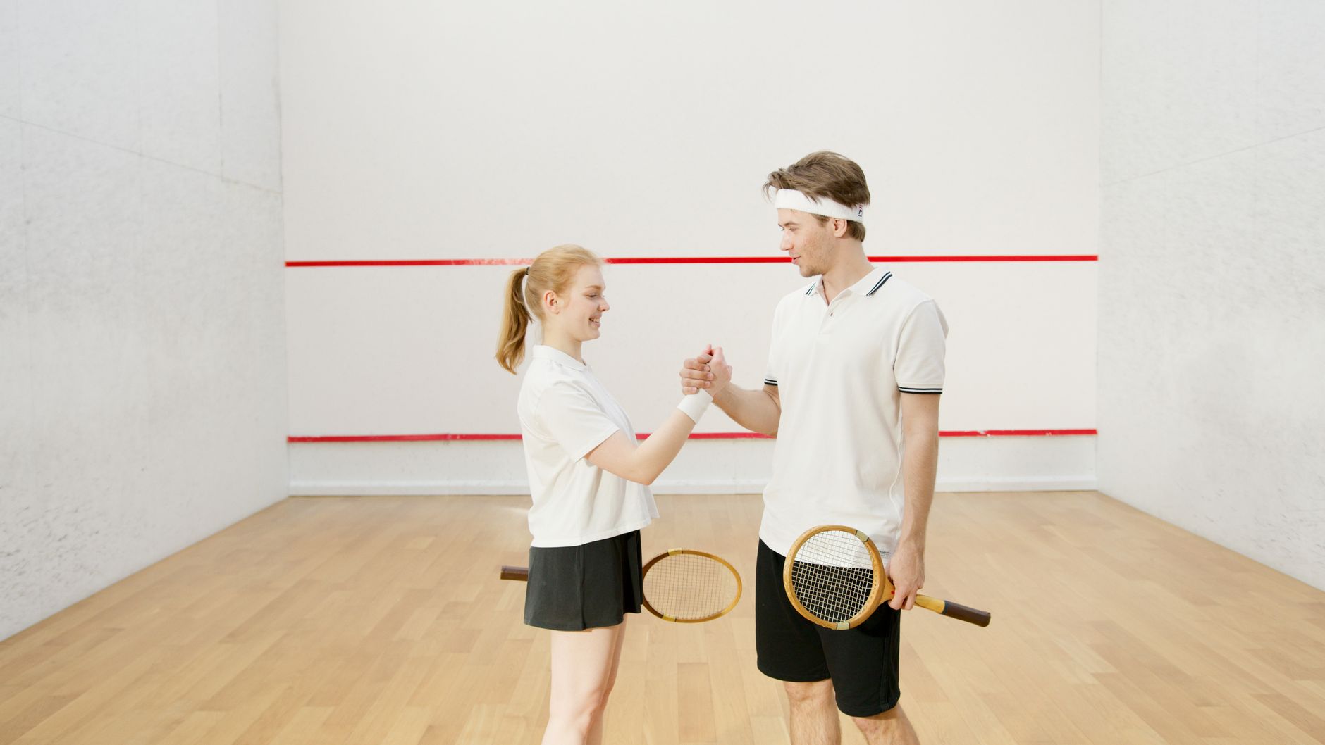 Smiling young adults playing squash indoors, demonstrating teamwork and sportsmanship.